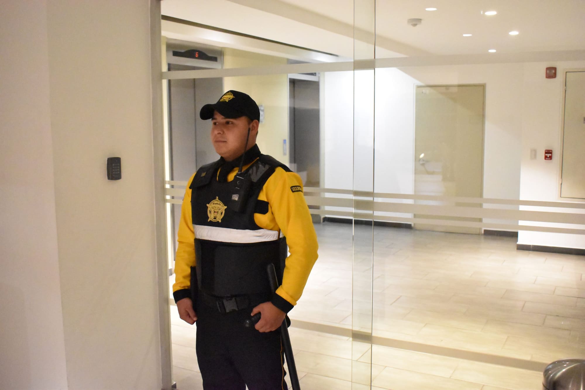 Guardia de Seguridad BAS en el lobby de un edificio, junto al lector del control de accesos y los ascensores.