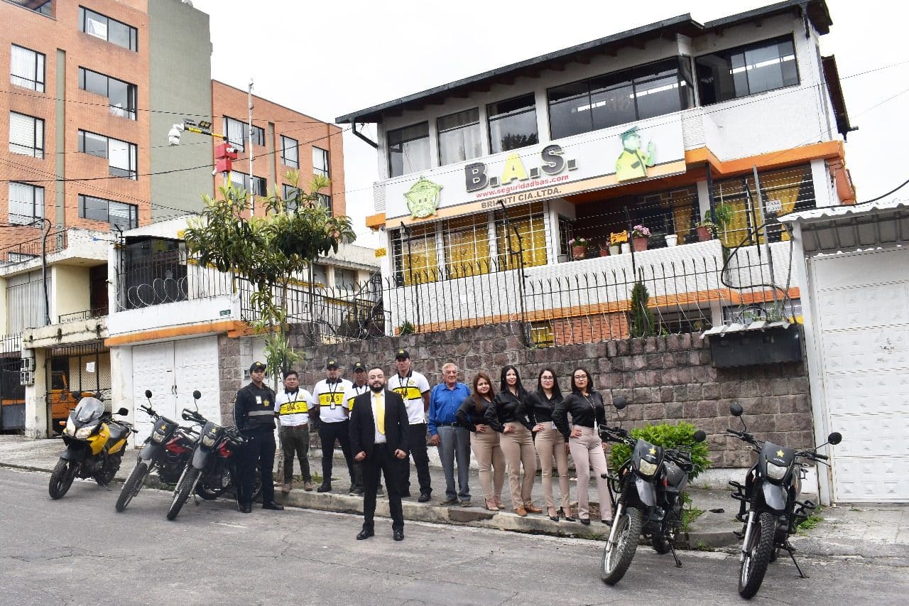 Equipo de Seguridad BAS —guardias uniformados, personal administrativo y motos de patrullaje— frente a la matriz de la empresa en Quito.